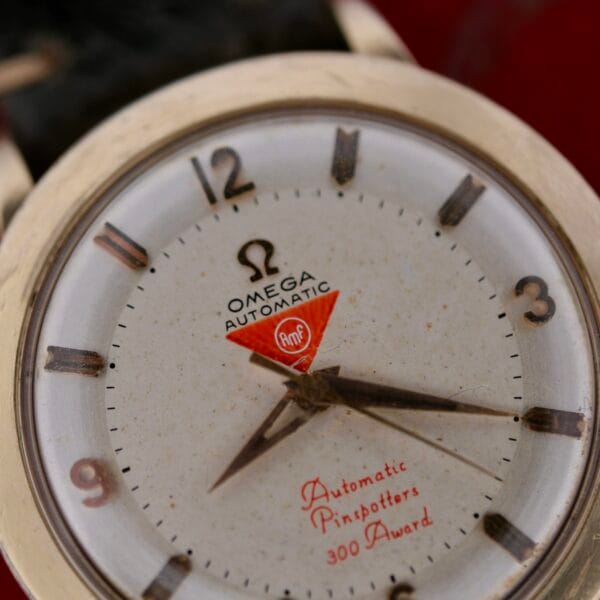 Close-up of an Omega Pinpointers 300 Game Dial Wristwatch Automatic. The dial features Arabic numerals, baton hands, and a red triangular AMF emblem with Automatic Pinspotters 300 Award. This vintage piece radiates a worn, classic elegance true to its heritage.