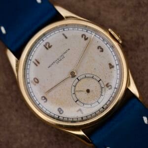 The Vacheron Constantin 18k Gold Caltrava Cal. V453 features a round gold case, cream dial with worn numerals, two hands, and a small subdial. It includes a blue leather strap and subtly displays VACHERON CONSTANTIN GENEVE, enhancing its timeless charm.