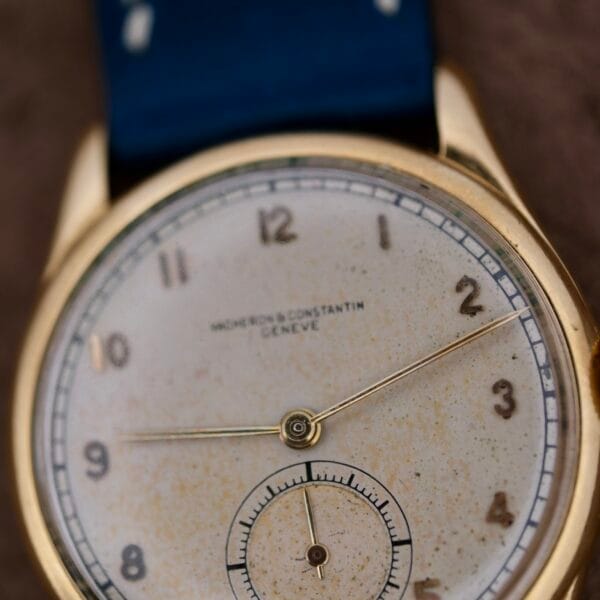 Close-up of a Vacheron Constantin 18k Gold Caltrava Cal. V453 watch with a gold case and blue strap, featuring a dial with aging spots, minimalistic hour markers and hands, plus a small seconds subdial at 6 oclock.