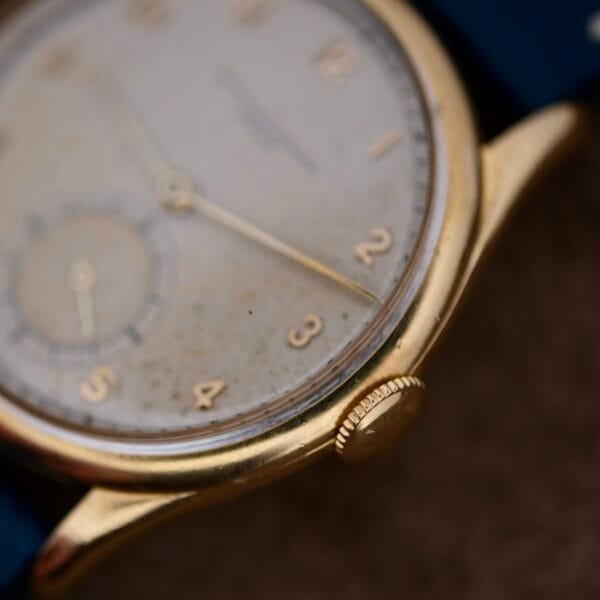 A close-up of the Vacheron Constantin 18k Gold Caltrava Cal. V453 reveals its vintage charm with Arabic numerals 1 to 5, a small seconds sub-dial, and a worn dial. The dark blue strap peeks through its aged gold casing, exuding timeless elegance and stories of yesteryears.