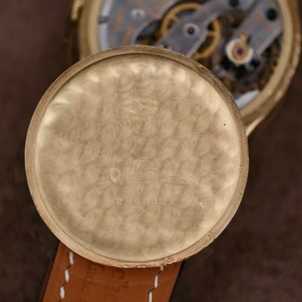 Close-up of an open Vacheron Constantin 18k Gold Caltrava Cal. V453 pocket watch, revealing intricate gears and mechanisms. The inside cover displays engraved markings and numbers, enhancing its timeless charm as it rests elegantly on a brown leather surface.