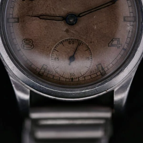 Close-up of the Omega WWII Era Military Sub Seconds watch, showcasing its vintage design with a worn brown dial, Arabic numerals 8 and 4, a small seconds subdial at 6 oclock, and a silver metal case and bracelet.