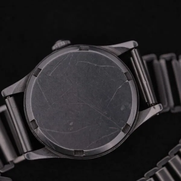 Close-up of an Omega WWII Era Military Sub Seconds watch, with a scratched metal case and strap featuring a brushed finish, resting on a dark surface.