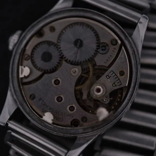 A close-up of the Omega WWII Era Military Sub Seconds watch reveals intricate internal mechanisms, showcasing Swiss craftsmanship. The metallic finish and metal bracelet enhance its visible engravings, epitomizing classic elegance.