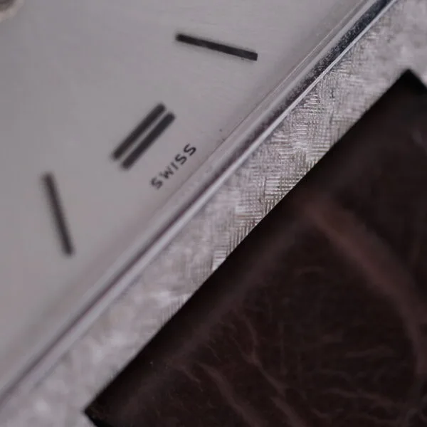 A close-up of the Vacheron Constantin 6761 Cal 1003 watch showcases the SWISS text on its textured silver dial, highlighting the craftsmanship and featuring part of a brown strap.