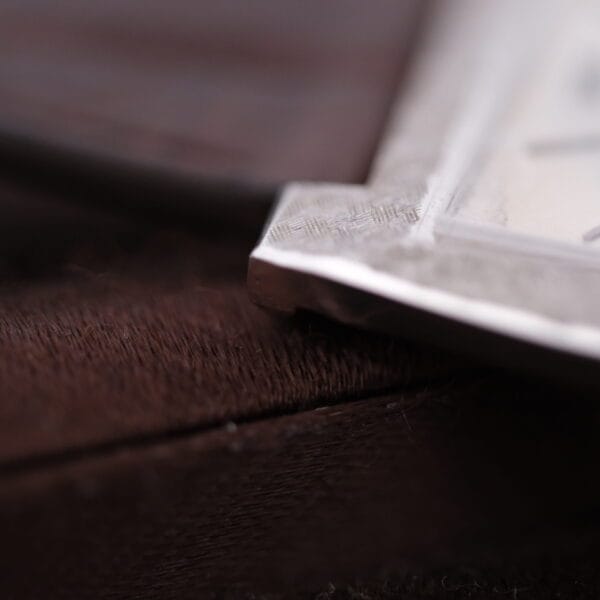 Close-up of a metallic corner from a Vacheron Constantin 6761 Cal 1003, resting on a textured brown surface. The focus highlights the intricate metal patterns along the edge.