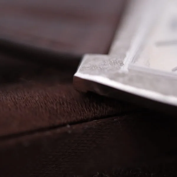 Close-up of a metallic corner from a Vacheron Constantin 6761 Cal 1003, resting on a textured brown surface. The focus highlights the intricate metal patterns along the edge.