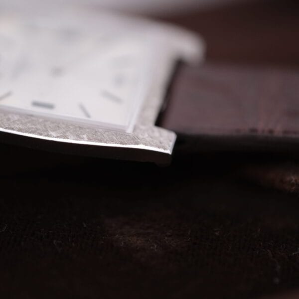 Close-up of a Vacheron Constantin 6761 Cal 1003 square watch face with polished silver frame and brown leather strap, slightly out of focus, resting on a dark surface.