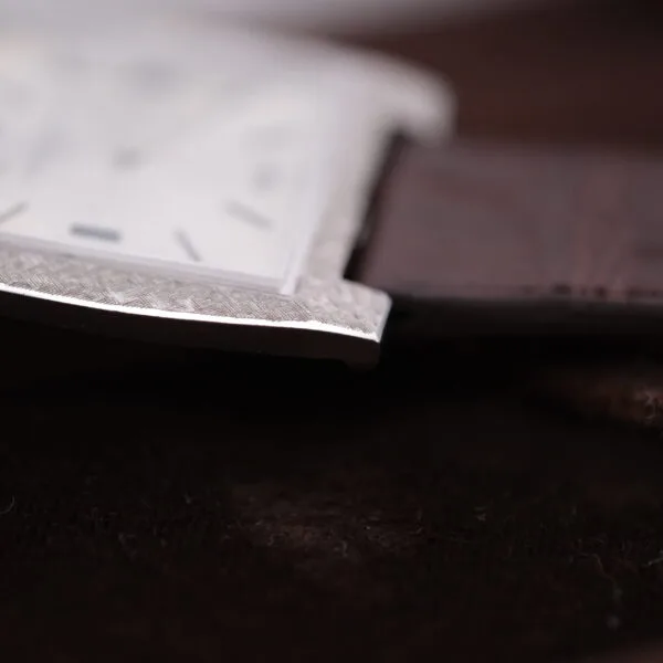 Close-up of a Vacheron Constantin 6761 Cal 1003 square watch face with polished silver frame and brown leather strap, slightly out of focus, resting on a dark surface.
