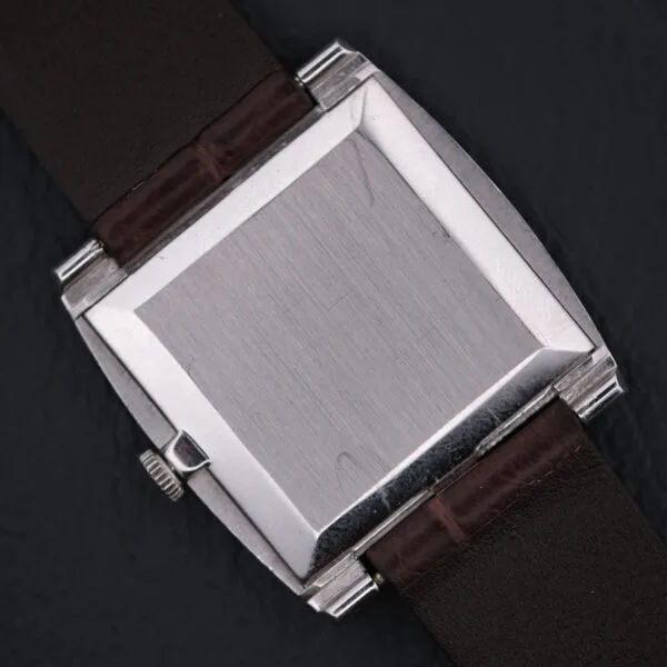 A silver square watch case with a dark brown leather strap is set against a dark background. The blank watch face subtly reflects light, reminiscent of the refined elegance of the Vacheron Constantin 6761 Cal 1003, exuding timeless sophistication.