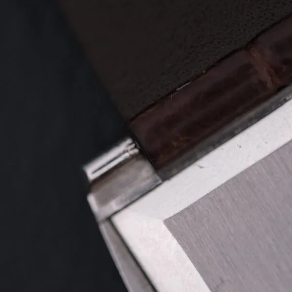 Close-up of a metal and brown leather corner, echoing Vacheron Constantin 6761 Cal 1003 craftsmanship. Precise stitching and sharp edges contrast the smooth metallic surface with rugged leather textures.