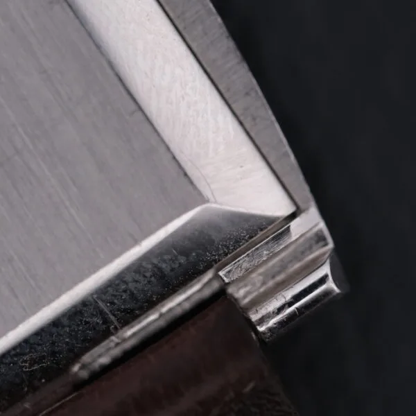 Close-up of an angular, metallic corner of a sleek, brushed steel Vacheron Constantin 6761 Cal 1003 with subtle reflections on its surface against a dark background, highlighting the precision and craftsmanship.