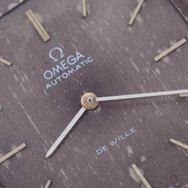 Close-up of a 1974 Omega Deville Automatic TV Case Ref. 151.0044 watch face, featuring the brand name with gold hour markers and hands. The word De Ville elegantly graces the bottom, highlighting its timeless sophistication.