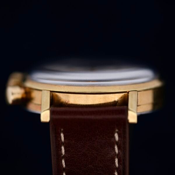 Close-up side view of the Omega Seamaster Chronograph Ref. 105.005 321 Caliber with a gold-toned case and brown leather strap with white stitching. Focus is on the edge and strap against a dark background, highlighting its elegance.