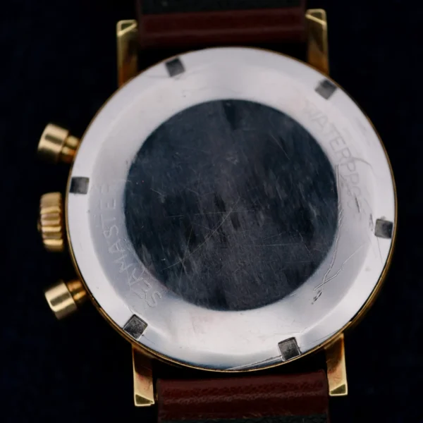 The image features the back of an Omega Seamaster Chronograph Ref. 105.005 321 Caliber wristwatch, with a round metal case. Seamaster and Waterproof are engraved on it. It has a leather strap, two side crowns, and displays light scratches on the metal.