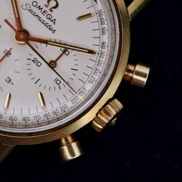 A close-up of the Omega Seamaster Chronograph Ref. 105.005 321 Caliber watch showcases its elegant gold-toned bezel and white dial, adorned with subdials and a tachymetric scale. The Seamaster name is prominently displayed, reflecting its prestigious craftsmanship.