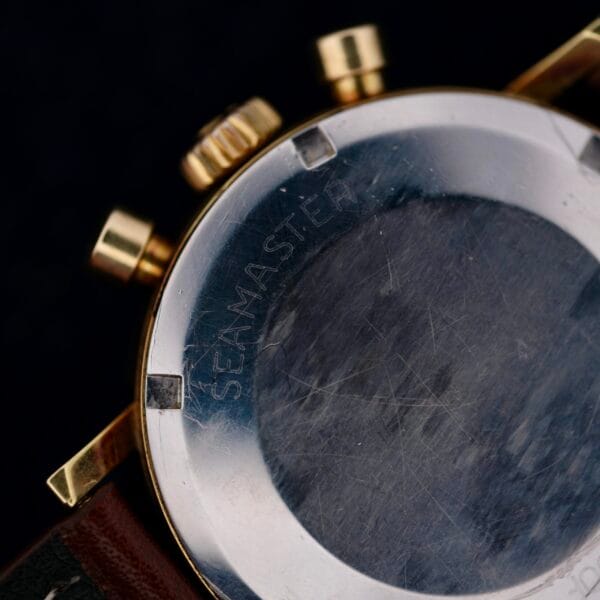 Close-up of an Omega Seamaster Chronograph Ref. 105.005 321 Caliber, highlighting SEAMASTER engraved on the back. This classy watch has a brown leather strap and gold accents on the side, with a subtly scratched surface.