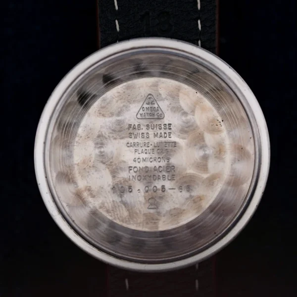 The image shows the interior of an Omega Seamaster Chronograph Ref. 105.005 321 Caliber watch case back with engravings like Fab. Suisse, Swiss Made, and Omega Watch Co., featuring a circular, textured pattern inside.