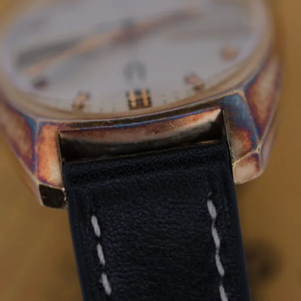 Close-up of a Bulova Accutron Day/Date wristwatch with an oxidized gold casing and black leather strap. The weathered edges enhance its vintage charm, and the blurred background highlights the intricate details of this classic timepieces structure.