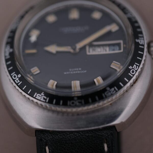 Close-up of the Caravelle Automatic Ref 745 Diver Jet Seconds Super Waterproof watch featuring a dark face, luminescent hands, day-date display, metal case, black bezel with white numerals, and a dark leather strap.