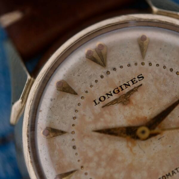 Close-up of a Longines Automatic Caliber 19AS with warm patina and twisted lugs. The watch face exudes vintage charm with gold-colored markers and hands, beautifully paired with a classic brown leather strap.