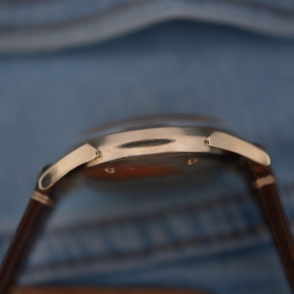 Close-up side view of the Longines Automatic Caliber 19AS with a silver case and brown leather strap on blue denim. The focus highlights its sleek form and detailed strap stitching.