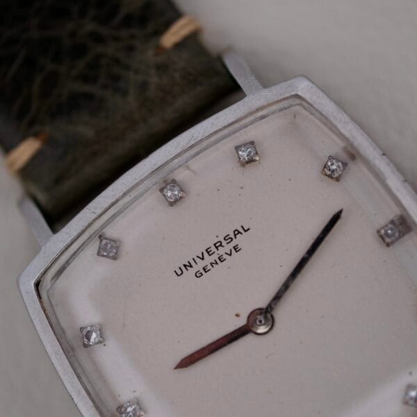 Close-up of a rectangular Universal Geneve White Diamond Dial Micro-Rotor Cal. 66 wristwatch with a white face, silver frame, and diamond hour markers, featuring two black hands and paired with a textured dark leather strap.