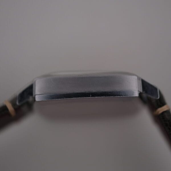 Side view of a Universal Geneve White Diamond Dial Micro-Rotor Cal. 66 wristwatch, featuring a sleek metal case and black leather strap, with its thin profile against a neutral background.