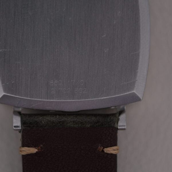 A close-up image reveals the back of a Universal Geneve White Diamond Dial Micro-Rotor Cal. 66 watch casing with engraved numbers. The top half shows partial engravings, while the timepieces dark brown leather strap enhances its elegant design.