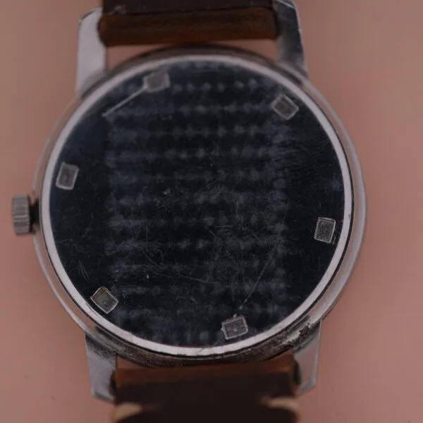 Close-up of a Girard Perregaux Sea Hawk wristwatch with a scratched black dial, silver case, and brown leather strap. The vintage watch lacks visible numbers, featuring only four small square markers at the 3, 6, 9, and 12 oclock positions.
