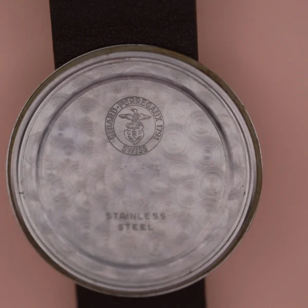 A close-up of the Girard Perregaux Sea Hawks back reveals engravings on its metal surface: Stainless Steel and a circular logo featuring an eagle alongside Girard-Perregaux 1791 Swiss, while the watch strap elegantly rests in the background.