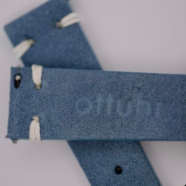 The Powder Blue Suede Watch Strap Vintage Stitch showcases a vintage flair with white stitching and features the embossed ottuhr brand name on a neutral background.