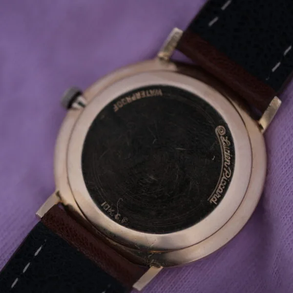 Back of a vintage Lucien Picard Seashark Automatic Slim Case in gold with a dark leather strap featuring white stitching on purple fabric, engraved with WATERPROOF and 10K G.F. for gold-filled material.