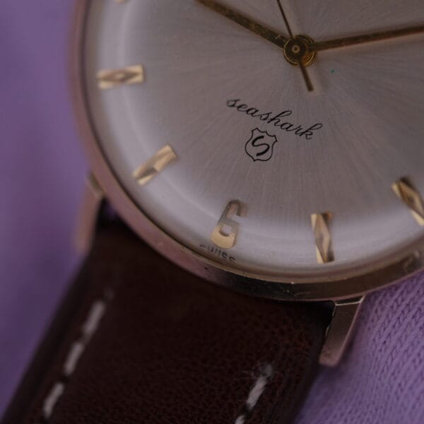 Close-up of a Lucien Picard Seashark Automatic Slim Case watch with a silver dial and gold hour markers, featuring a brown leather strap, resting on soft purple fabric.