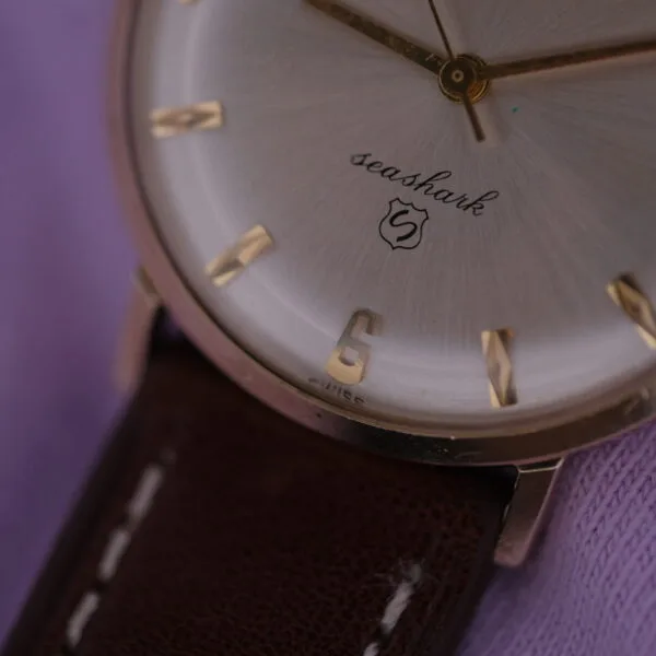 Close-up of a Lucien Picard Seashark Automatic Slim Case watch with a silver dial and gold hour markers, featuring a brown leather strap, resting on soft purple fabric.