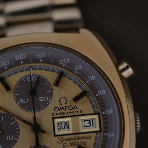 The 1975 Omega Speedsonic f 300Hz Chronograph Ref. 188.0002 boasts a detailed watch face with three sub-dials, a day-date window displaying SUN and 31, and the unique 300 Hz marking, all set to about 10:09 against its elegant gold and silver metallic band.