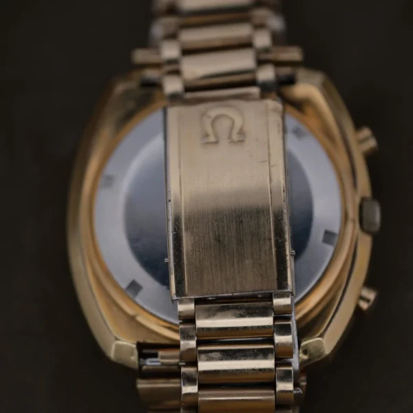 Close-up image of a gold 1975 Omega Speedsonic f 300Hz Chronograph Ref. 188.0002 wristwatch with a metal bracelet and an engraved Omega logo clasp, partially obscuring the elegant watch face.