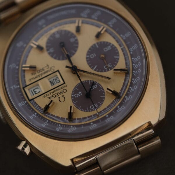 Close-up of a 1975 Omega Speedsonic f 300Hz Chronograph Ref. 188.0002 with gold casing and intricate details, featuring multiple dials and day/date display. The metal bracelet complements its elegant design.