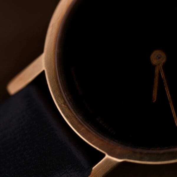 Close-up of a Ladies Movado Zenith 14k Gold Museum Dial wristwatch with a dark, minimalistic dial. Features gold casing, black leather strap, and time set near 10 oclock.