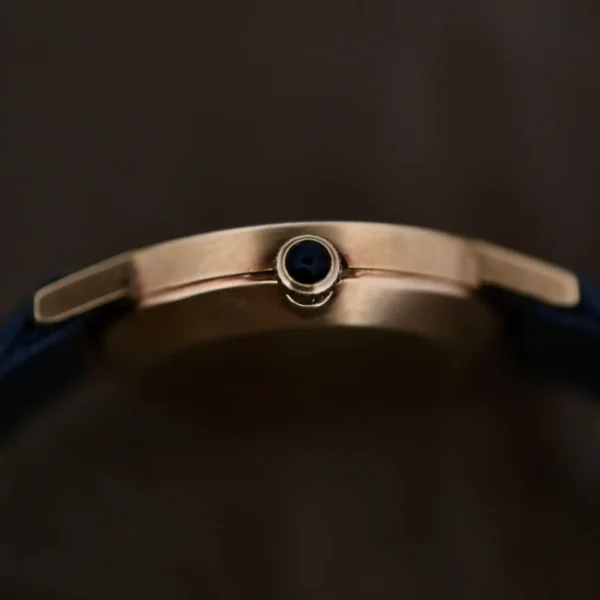 Close-up side view of a Ladies Movado Zenith 14k Gold Museum Dial watch case with a dark blue crown, set against a dark background. A blue strap is partially visible, attached to the Zenith-inspired case.