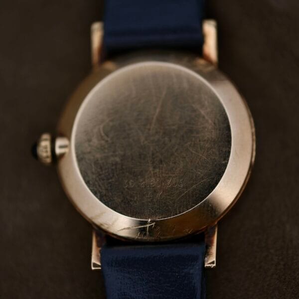 A close-up of the back of a vintage Ladies Movado Zenith 14k Gold Museum Dial watch with a navy blue leather strap. The back shows faintly engraved numbers and letters, while the metal casing has a worn appearance, exuding timeless elegance.