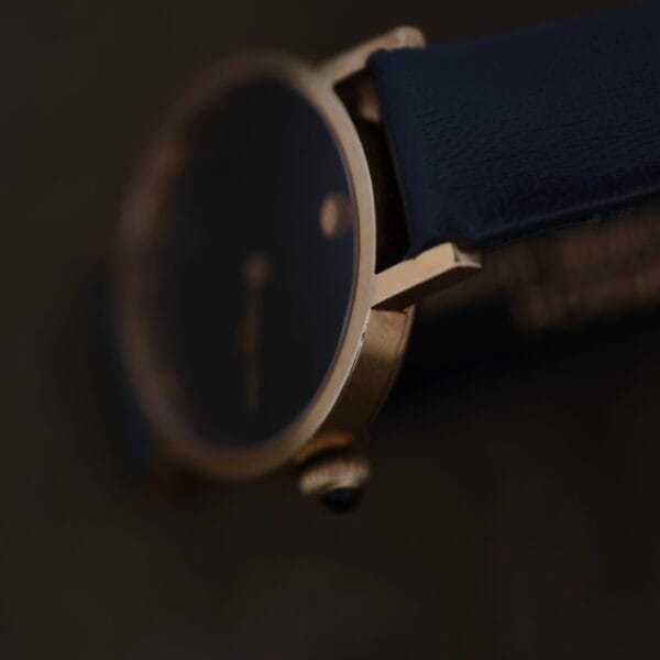 Close-up of a Ladies Movado Zenith 14k Gold Museum Dial wristwatch, featuring a dark face with a navy blue strap. The image showcases its elegant and minimalist design.