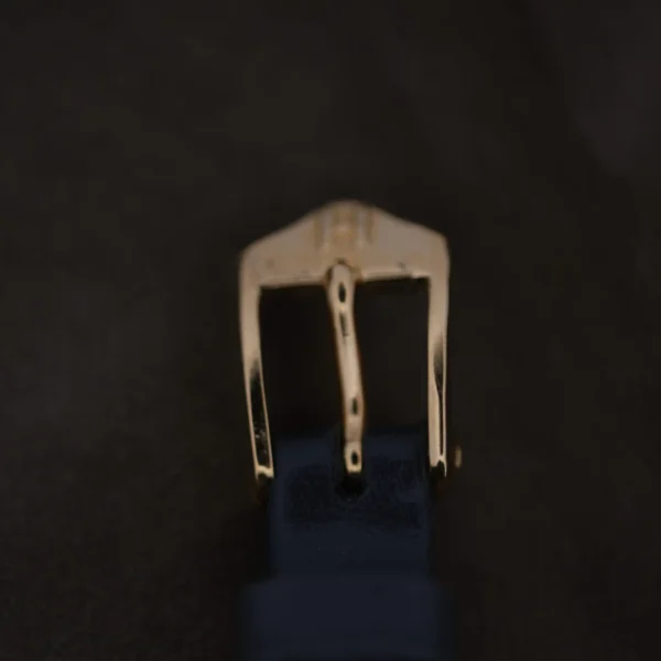 Close-up of a Ladies Movado Zenith 14k Gold Museum Dial watch buckle on a dark blue strap against a darker background, with the metallic finish and intricate details in sharp focus.