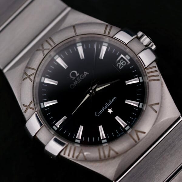 The Omega Constellation Ref. 396.201 features a black dial with the Omega logo and Constellation branding, silver Roman numerals, and a 3 oclock date window, complemented by its stainless steel bracelet.