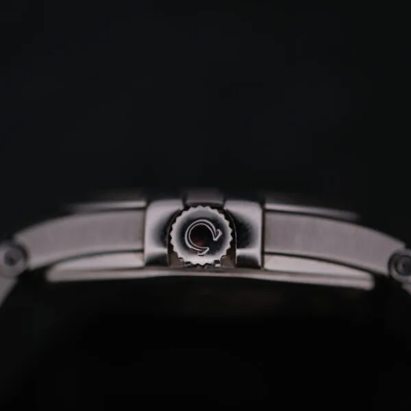 A close-up of the Omega Constellation Ref. 396.201 crown, featuring a logo, set against a dark backdrop highlights the intricate stainless steel details and rotating mechanism of this watchs side.