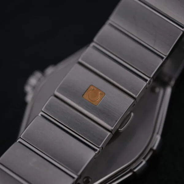 A close-up of the Omega Constellation Ref. 396.201 bracelet reveals its stainless steel and a gold emblem on the clasp, with a slightly reflective design standing out against a dark background, highlighting its sophistication.