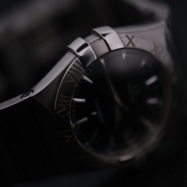 Close-up of the Omega Constellation Ref. 396.201, a luxury wristwatch with a polished metal bracelet and bezel, showcasing a partially visible face with Roman numerals and sleek design against a dark background.