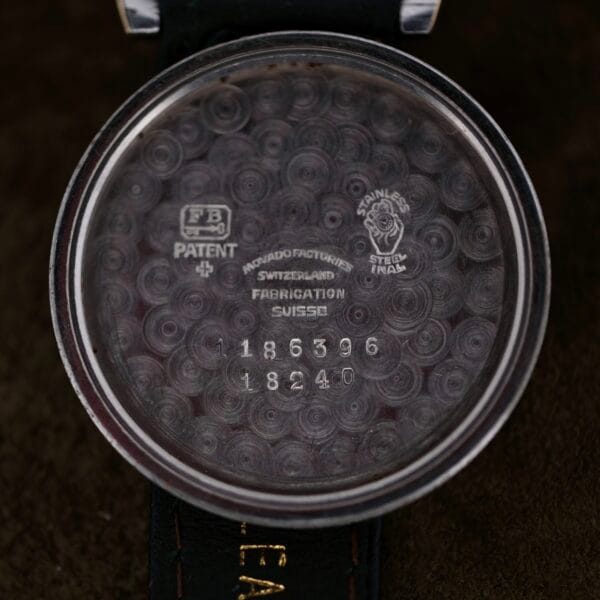 Close-up view of the inner back of a Movado Ref. 18240 Francois Borgel Gold Top watch for the Hong Kong market, featuring engraved text like FABRICATION SUISSE, PATENT, serial number 1186396, and a circular brushed metal texture.