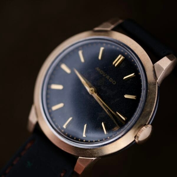 The vintage Movado Ref. 18240 Francois Borgel Gold Top Hong Kong Market wristwatch showcases a black face with gold hour markers and bezel, attached to a dark leather strap, with the brand name Movado elegantly displayed.