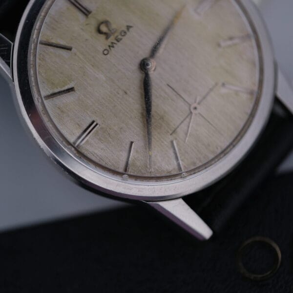 An Omega Manual Wind Cal. 268 wristwatch boasts a weathered dial with Roman numeral hour markers, complemented by a leather strap and metal case. The iconic Omega logo at 12 oclock highlights its timeless elegance and classic craftsmanship.